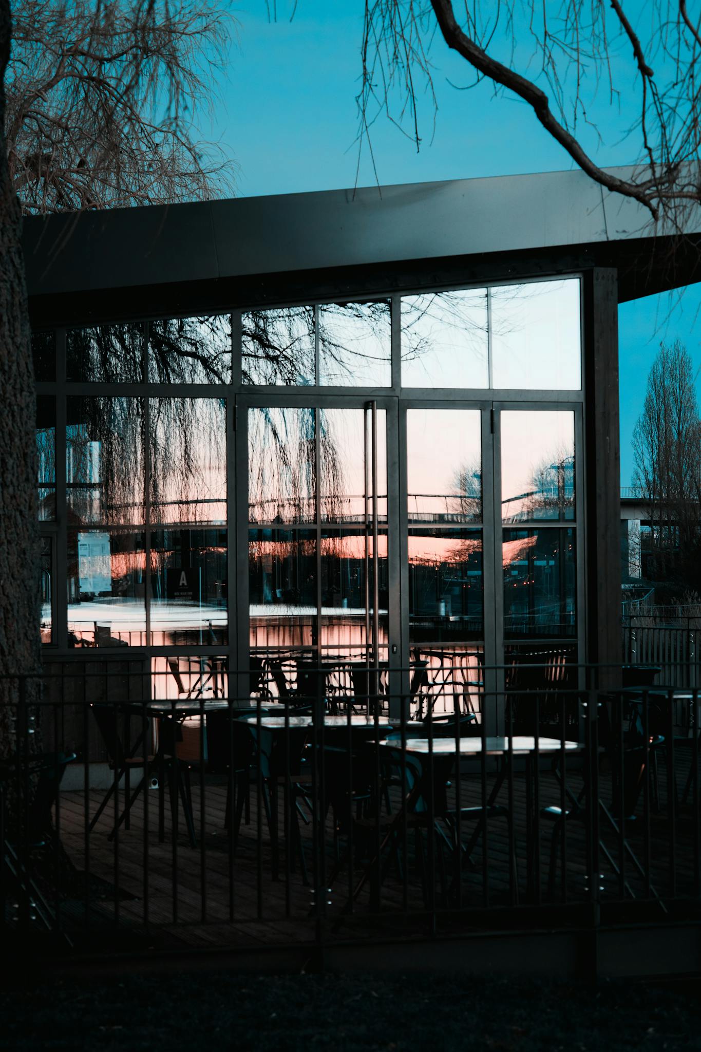 A modern building with glass windows reflecting the sunset view, featuring empty outdoor seating.